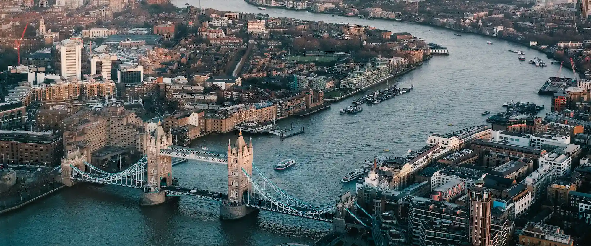Aerial view of London showing Tower Bridge over the Thames with surrounding buildings and boats on the river.