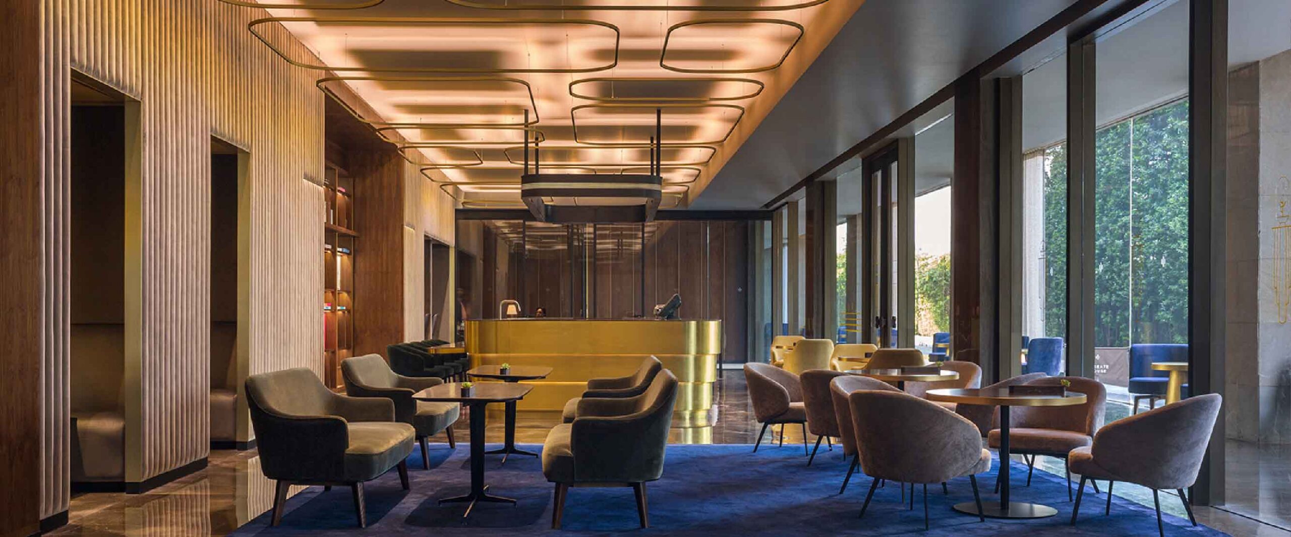 Luxurious hotel lobby with a gold reception desk, plush chairs, and geometric ceiling lighting.