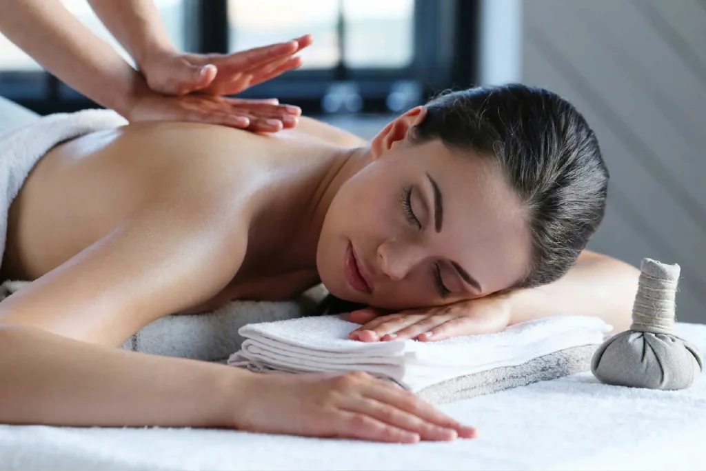 ayurveda-massage | The Roseate Ganges Rishikesh Woman lying face down on a massage table with eyes closed as a therapist massages her back in a spa setting.